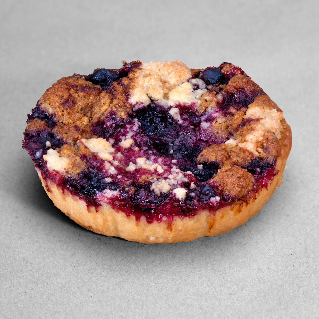 Tartelette saveur noisettes et myrtilles posée sur un fond gris