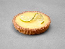 Tartelette citron avec une tranche de citron pour décor posée sur un fond gris