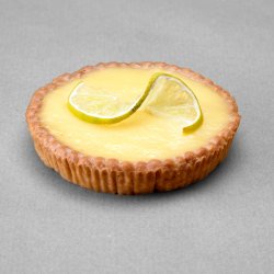 Tartelette citron avec une tranche de citron pour décor posée sur un fond gris