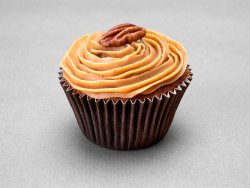 Muffin aux noix de pécan avec une ganache caramel et une noix comme décor posé sur un fond gris