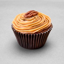Muffin aux noix de pécan avec une ganache caramel et une noix comme décor posé sur un fond gris